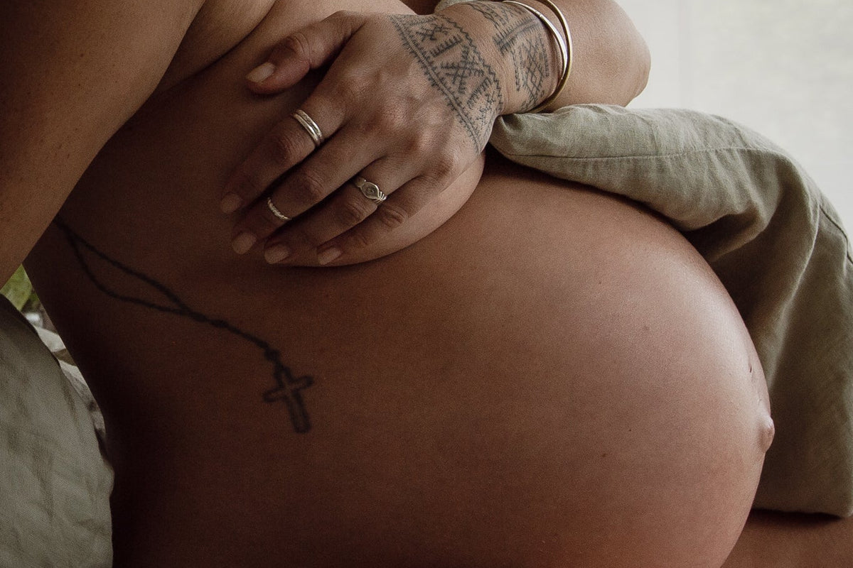 Person holding their pregnant belly with a soft, neutral background